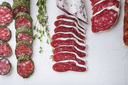 Variety of dry cured fuet and chorizosalami sausages, whole and sliced on white textured background, topview.