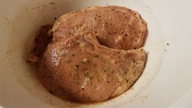seasoned pork chops with oil in white container or bowl