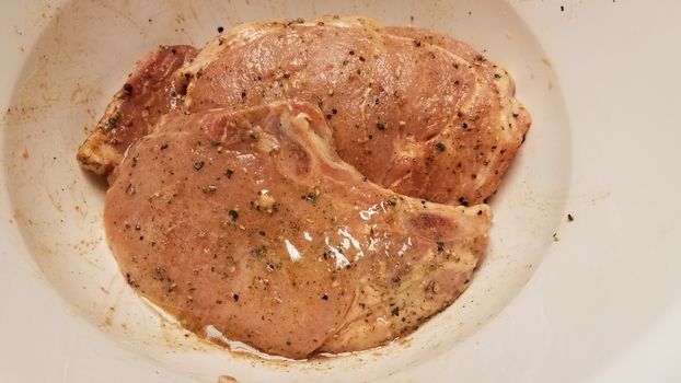 seasoned pork chops with oil in white container or bowl