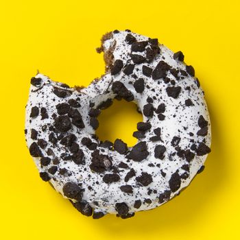 chocolate donut with white glaze isolated on yellow background, close up flat lay