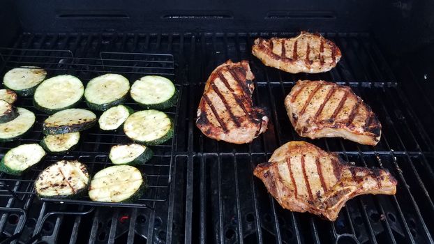 zucchini and pork chops cooking on barbecue grill