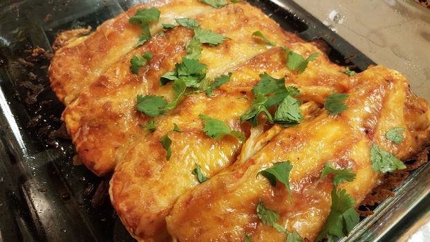 cheesy enchiladas with tortillas with cilantro in glass container on stove