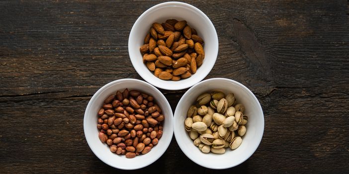 Pistachio, peanut and almond in a small plates which standing on a black table. Nuts is a healthy vegetarian protein and nutritious food