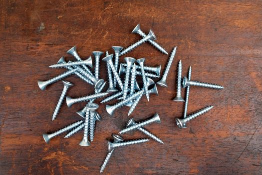 Heap of many light gray screws on brown wooden background top vieew closeup view