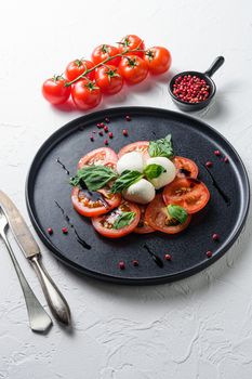 Caprese fresh italian salad with tomatoes, mozzarella, green basil on dark slate plate over white background close up selective focus vertical.