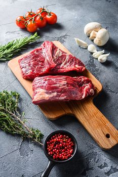 Raw flap steak flank cut with Machete, Skirt Steak, on woods chopping board, with herbs tomatoes peppercorns over grey stone surface background side view.