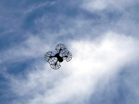 Drone contour with engine protection grid flying in the blue sky with calm white clouds view bottom to top