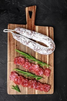 Fuet salami wurst cut in slices and whole sausage on black background, top view.