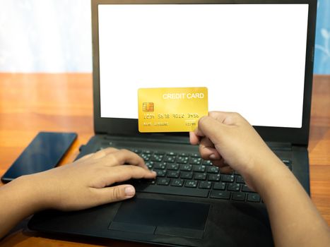 Close up human hand holding a credit card on a notebook background And the phone lay on table. Online shopping concept.
