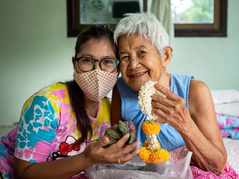 Image of a woman wearing a protective mask and a grandmother with a flower garland. Mother's day concept.