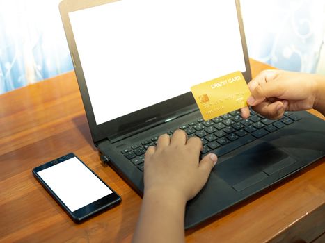 Close up human hand holding a credit card on a notebook background And the phone lay on table. Online shopping concept.