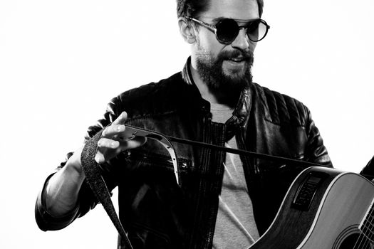 A man plays the guitar in a black leather jacket with sunglasses on a light background. High quality photo