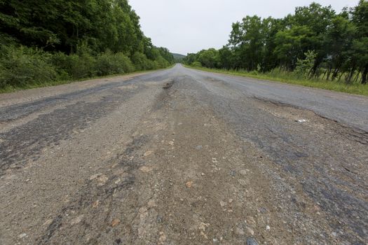 Very bad road in Russia. The asphalt road is all in holes in the middle of the forest