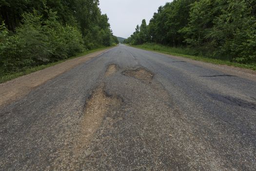 Very bad road in Russia. The asphalt road is all in holes in the middle of the forest