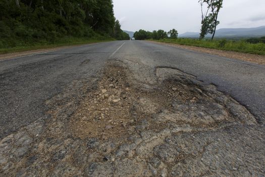 Very bad road in Russia. The asphalt road is all in holes in the middle of the forest