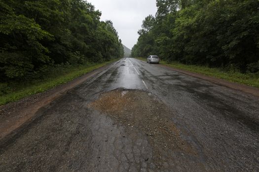 Very bad road in Russia. The asphalt road is all in holes in the middle of the forest