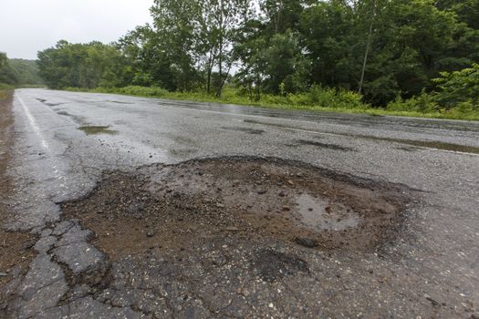 Very bad road in Russia. The asphalt road is all in holes in the middle of the forest