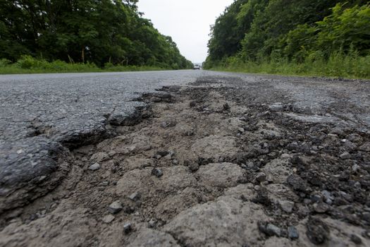 Very bad road in Russia. The asphalt road is all in holes in the middle of the forest