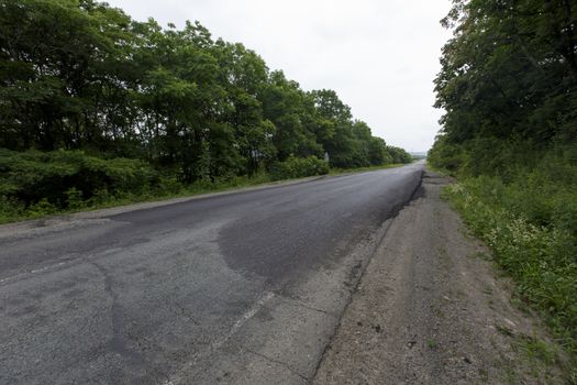 Very bad road in Russia. The asphalt road is all in holes in the middle of the forest