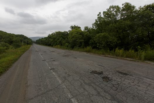 Very bad road in Russia. The asphalt road is all in holes in the middle of the forest