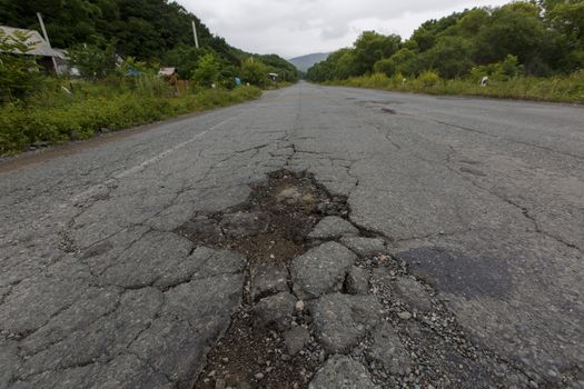 Very bad road in Russia. The asphalt road is all in holes in the middle of the forest