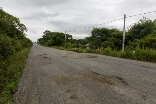 Very bad road in Russia. The asphalt road is all in holes in the middle of the forest