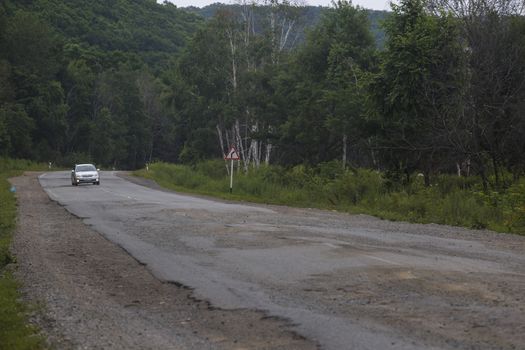 Very bad road in Russia. The asphalt road is all in holes in the middle of the forest