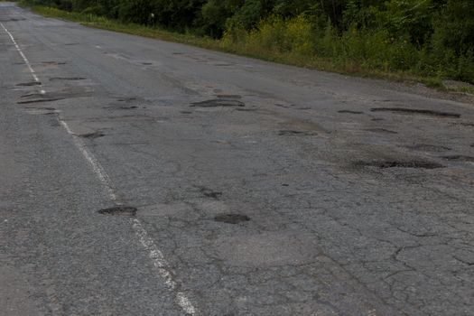 Very bad road in Russia. The asphalt road is all in holes in the middle of the forest