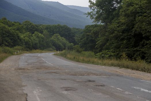 Very bad road in Russia. The asphalt road is all in holes in the middle of the forest