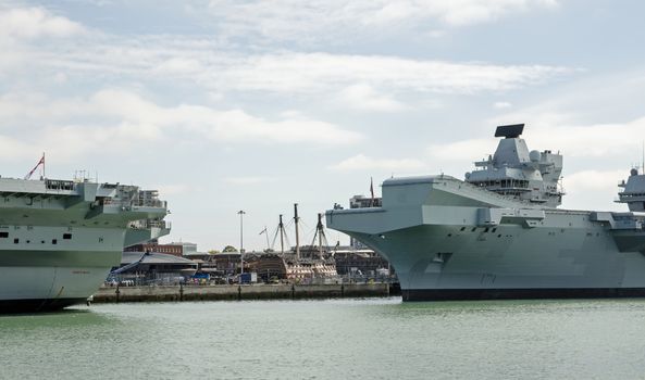 The historic HMS Victory on display at Portsmouth Historic Dockyard viewed between the Royal Navy aircraft carriers HMS Prince of Wales and HMS Queen Elizabeth on a sunny summer day.  