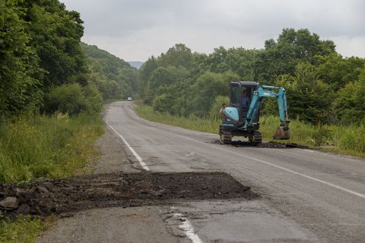 Repair of a bad road. Workers pave a bad road in a forest in Russia.