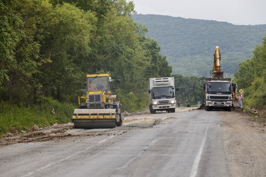 Repair of a bad road. Workers pave a bad road in a forest in Russia.