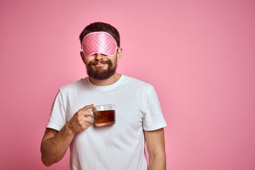 A man in a pink sleep mask with a cup of tea in his hands on an isolated background cropped view. High quality photo