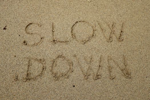 slow down, mindfulness concept written on sand.