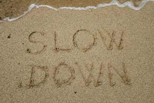 slow down, mindfulness concept written on sand.