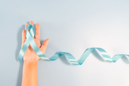 Prostate cancer awareness campaign concept, Men's health concept. hand holding light blue ribbon long tail on blue background. Symbol for support men who living with cancer
