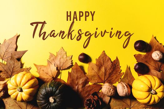 Happy Thanksgiving Day with maple leaves, nut and pumpkin on yellow background