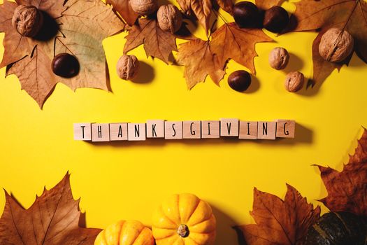 Happy Thanksgiving Day with maple leaves, nut, pumpkin and wooden cube on yellow background
