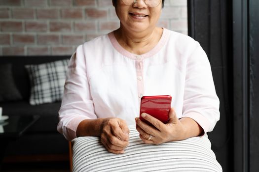 smiling senior woman using mobile phone while sitting on sofa at home