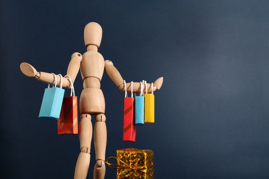 Cheerful happy shopaholic wooden doll with lots of shopping bags on arm