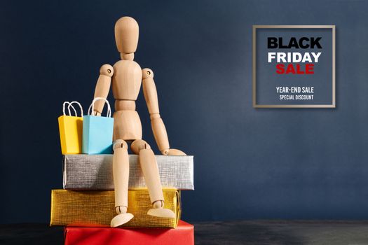 Black Friday sale, wooden doll sitting on gift box with shopping bag