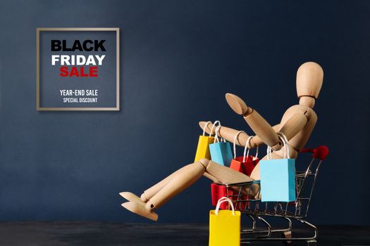 Black Friday sale, wooden doll sitting on shopping cart with shopping bag