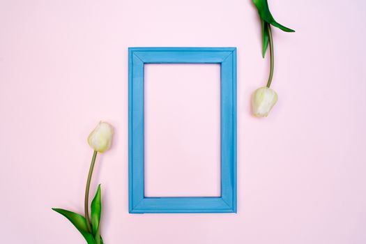 Flowers composition. tulip flowers with blue photo frame on pink background. Flat lay, top view, copy space