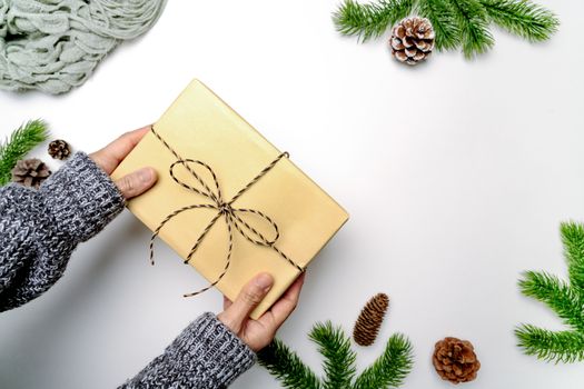 Christmas winter composition. Woman hand hold christmas gift box with pine cones, fir branches on white background. Flat lay, top view, copy space