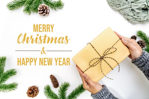 Christmas winter composition. Woman hand hold christmas gift box with pine cones, fir branches on white background. Flat lay, top view, copy space