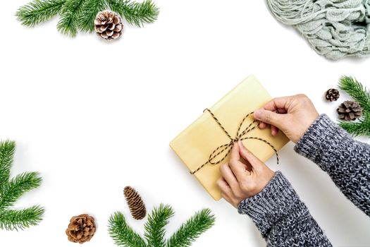 Christmas winter composition. Woman hands wrapping Christmas gifts box with pine cones, fir branches on white background. Flat lay, top view, copy space