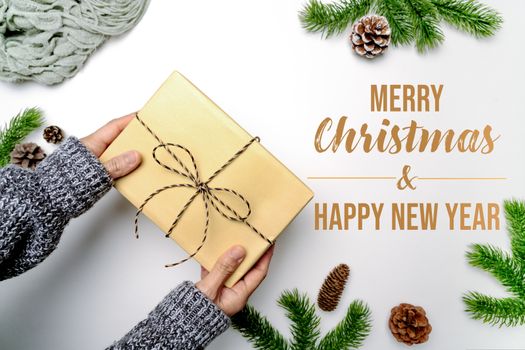 Christmas winter composition. Woman hand hold christmas gift box with pine cones, fir branches on white background. Flat lay, top view, copy space