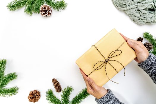 Christmas winter composition. Woman hand hold christmas gift box with pine cones, fir branches on white background. Flat lay, top view, copy space