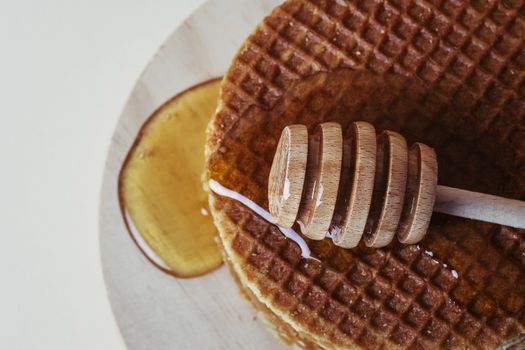 Honey dipper pouring honey over a pile of waffles on a wooden tray. Top view.