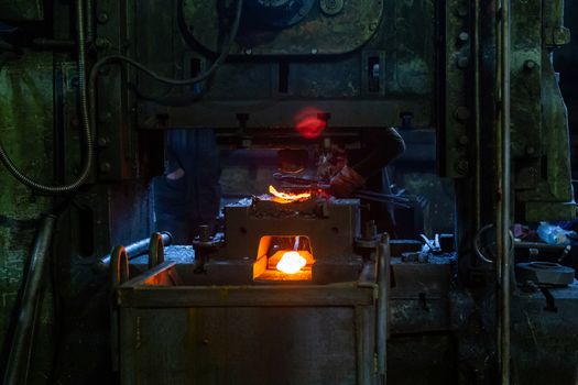 Close-up picture of fresh forged hot steel workpieces after press forming in dirty dark factory. Selective focus on foreground.